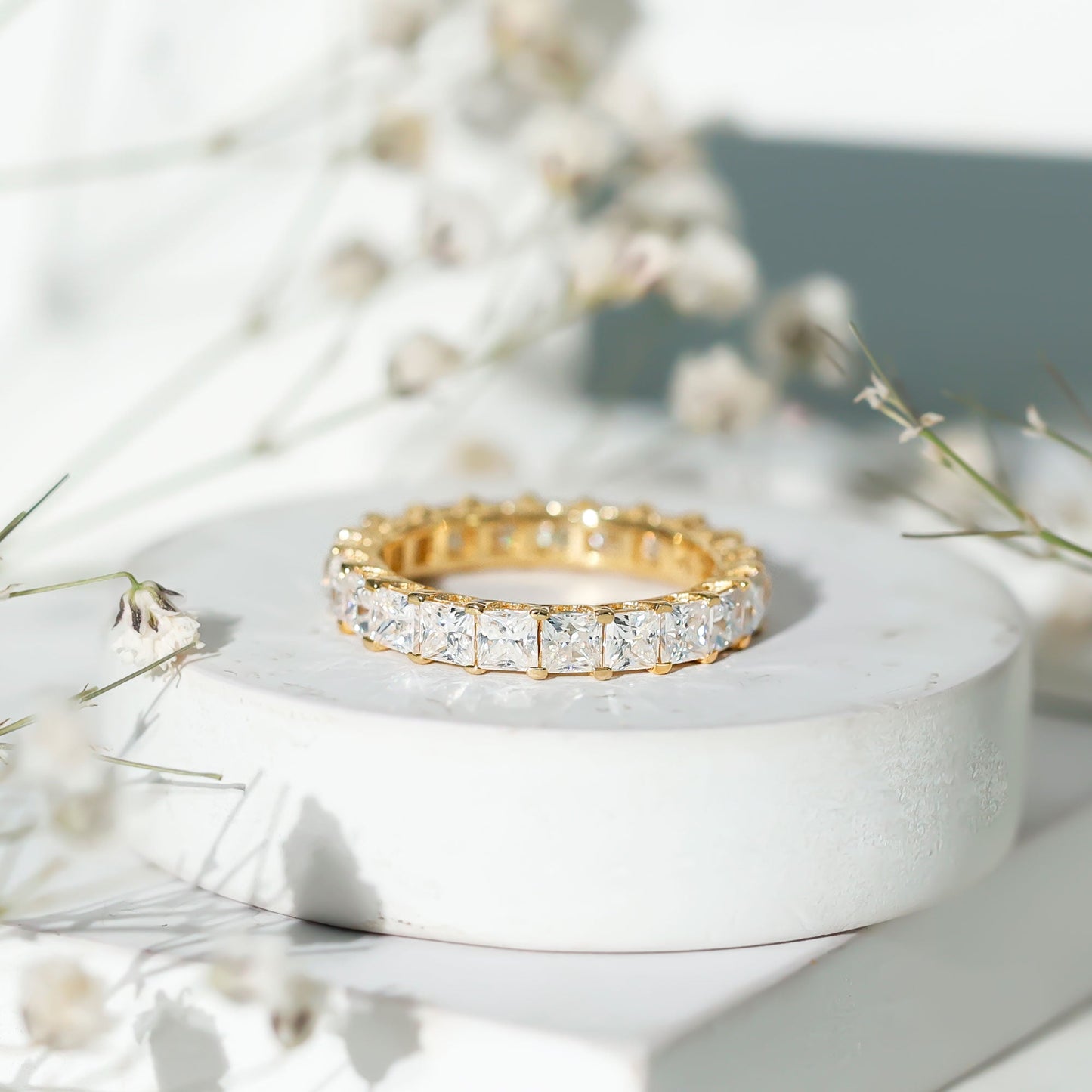 Gold ring with diamonds on a white stone surface with flowers in the background