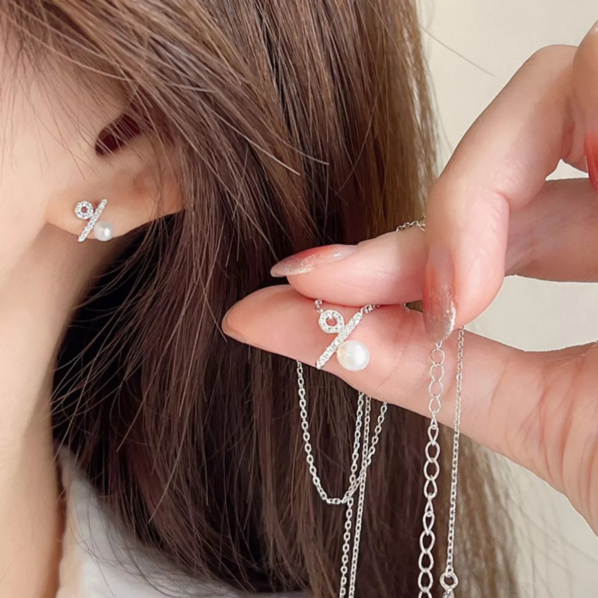 Close-up of a person wearing a silver earring with a pearl detail, holding a matching necklace.
