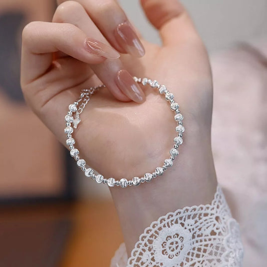 Hand wearing a delicate silver bracelet with blurred background