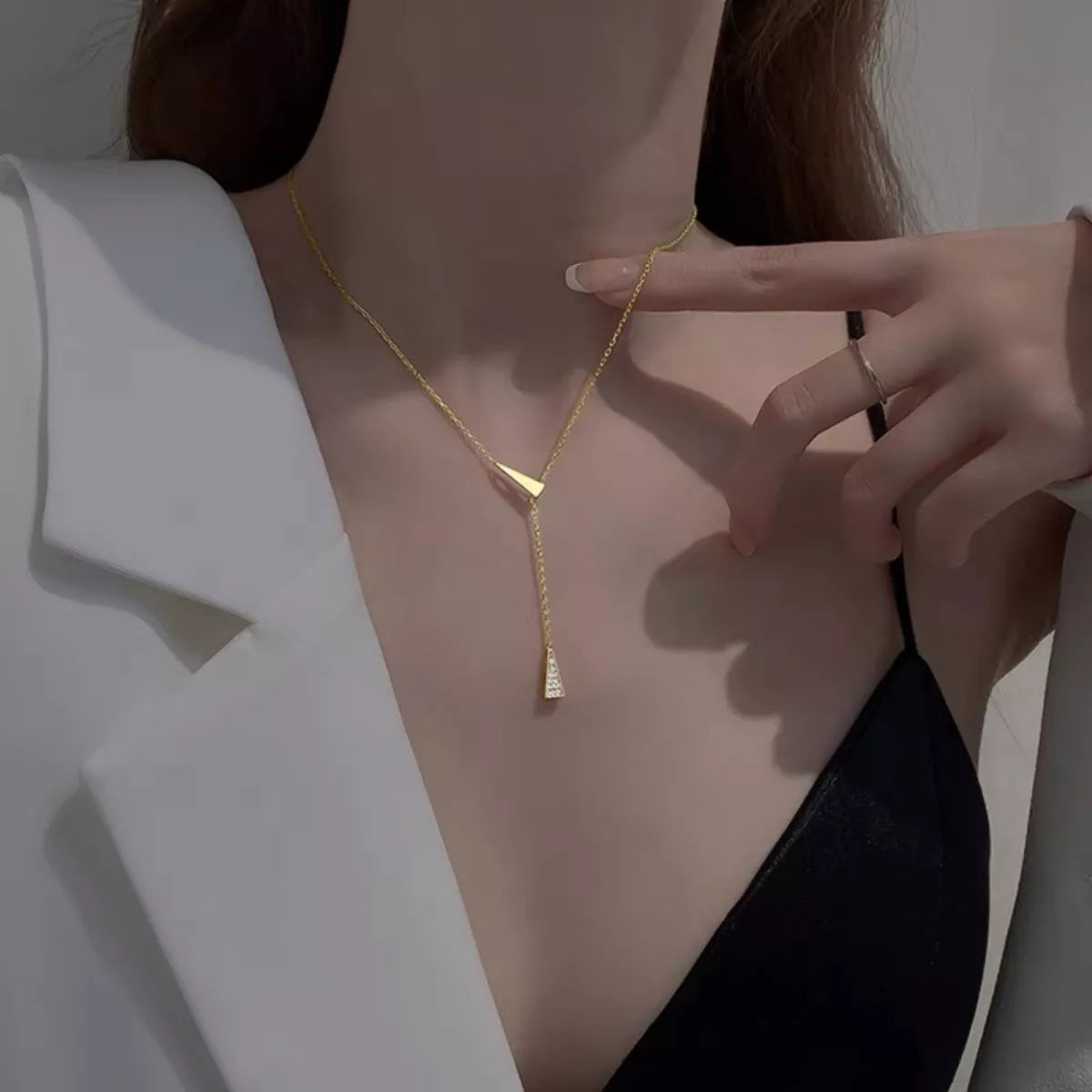 Gold necklace being worn and adjusted by a person against a neutral background