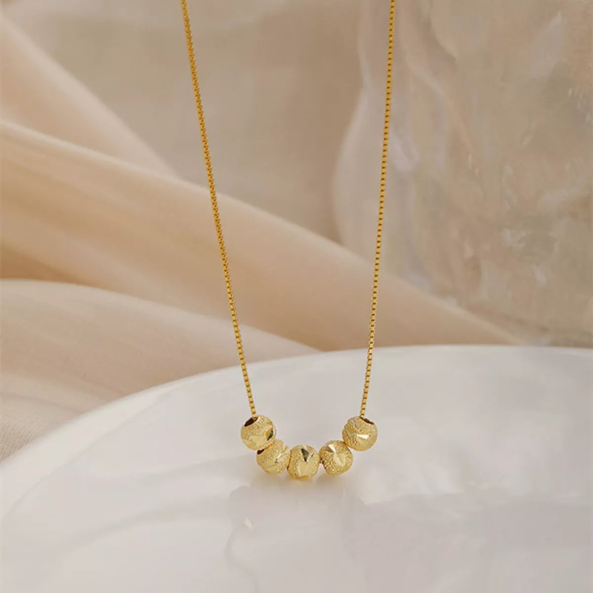 Gold necklace with beaded design on a soft beige background
