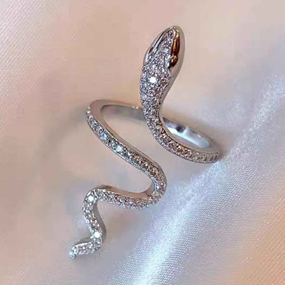 Silver snake-shaped ring with gemstones on a soft fabric background