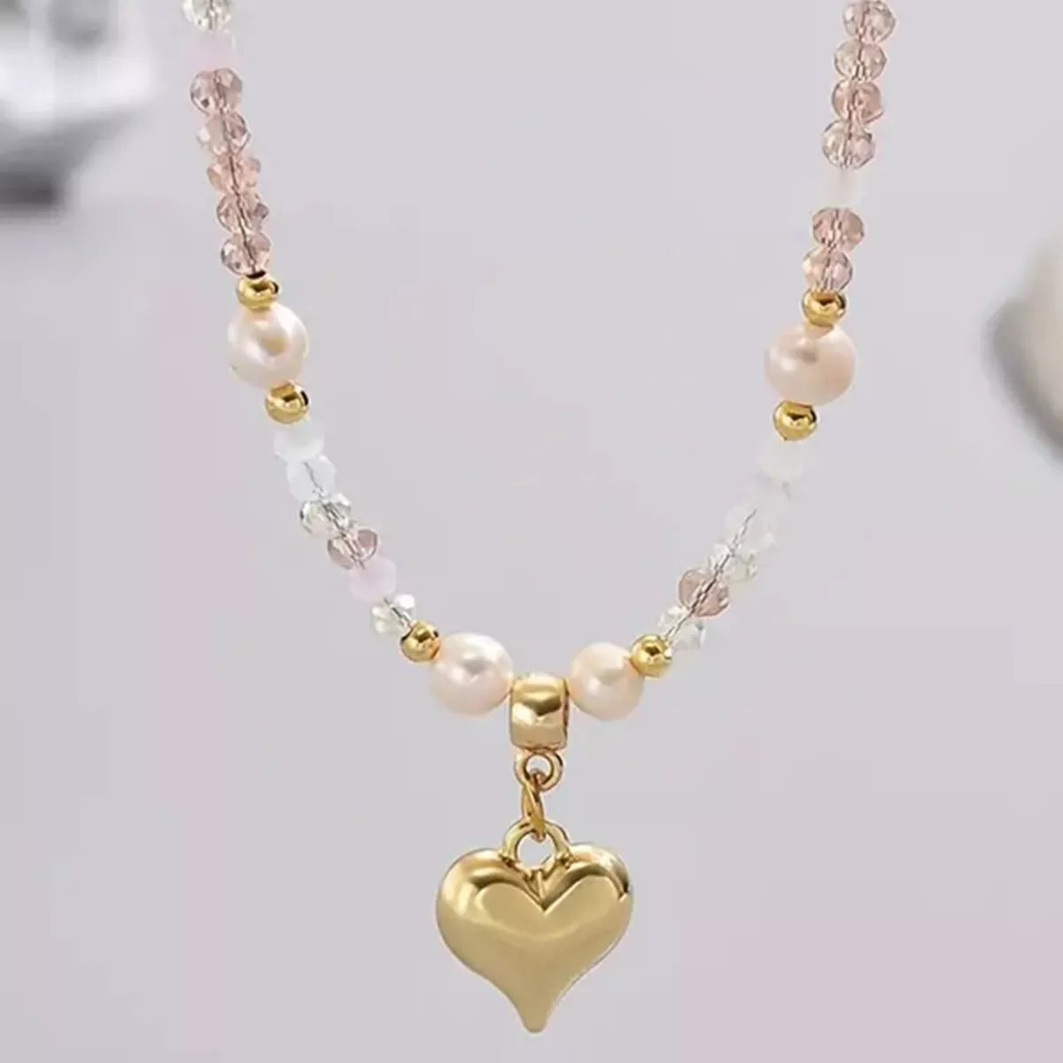 Necklace with heart-shaped gold pendant and pearl beads on a light gray background