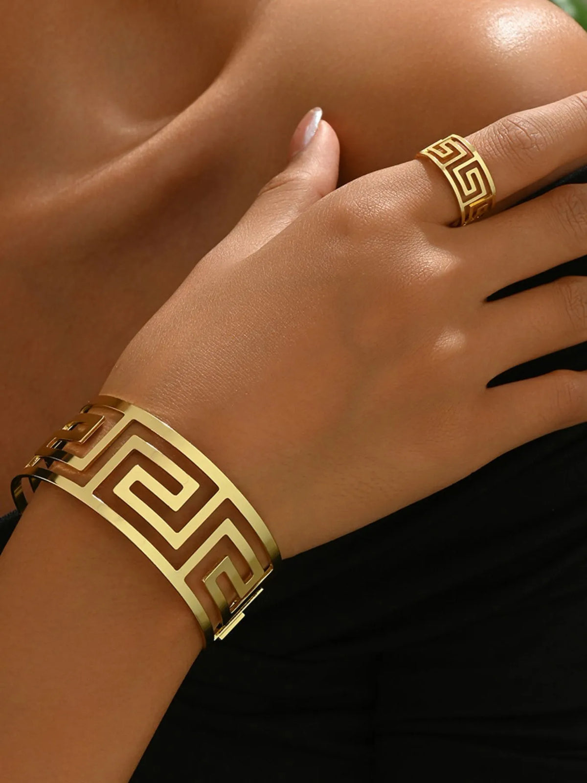 Gold bracelet and ring on a hand against a black background