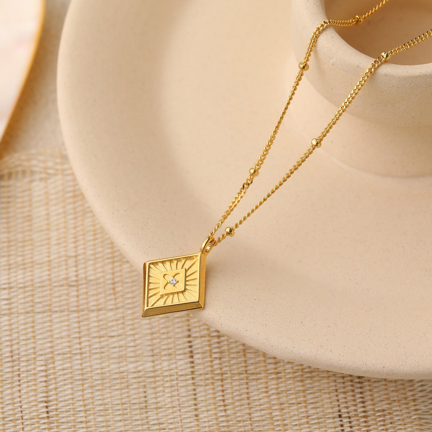 Gold necklace with a square pendant on a beige surface
