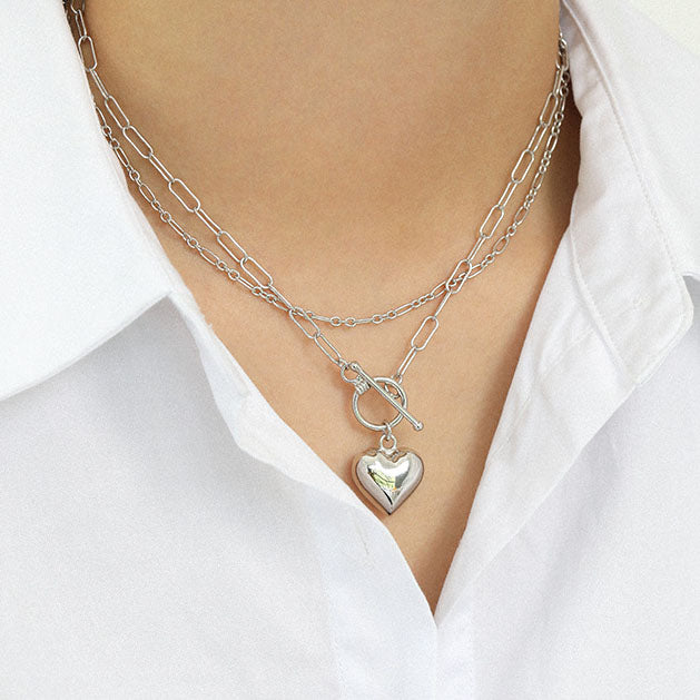 Silver necklace with a heart pendant worn by a person in a white shirt.