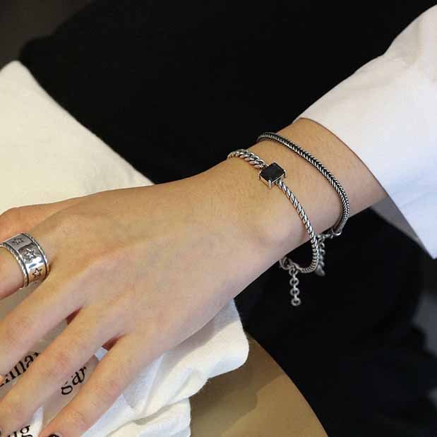 Close-up of a wrist wearing multiple silver bracelets and a ring on a white background