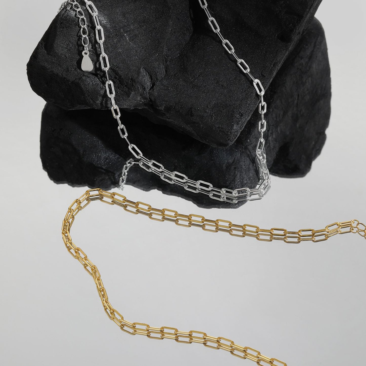 Gold and silver chain necklaces on a gray background with black stones.