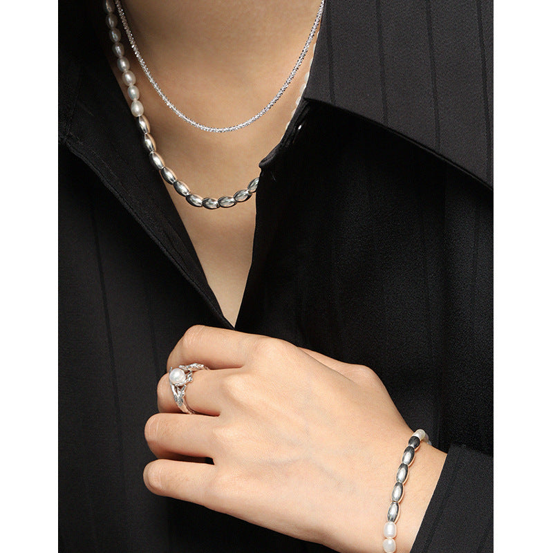 Person wearing a pearl necklace, ring, and bracelet on a black background