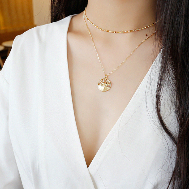 Gold necklace with a circular pendant worn by a person in a white outfit.