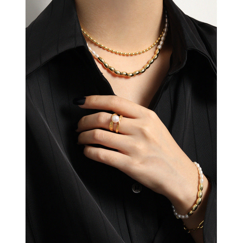 Close-up of a person wearing gold necklaces, a ring, and a bracelet on a black shirt.