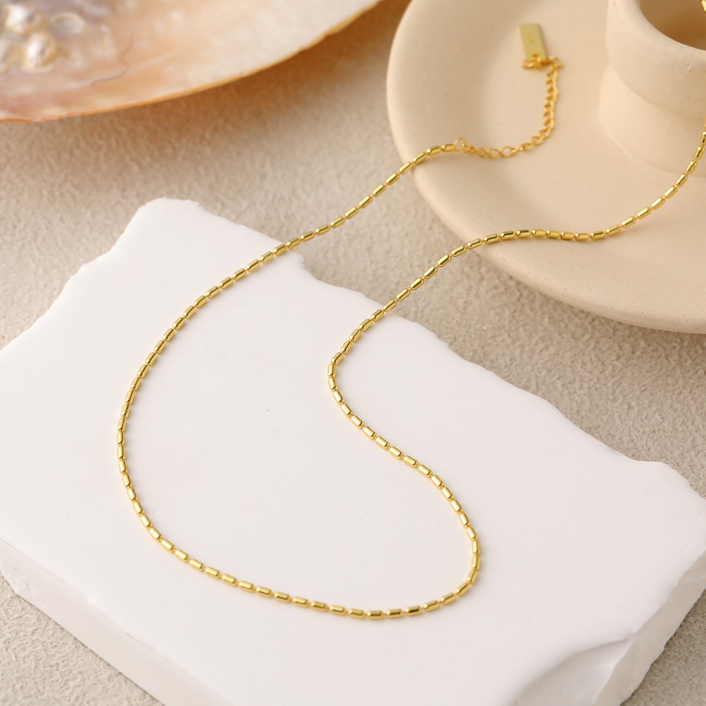 Gold chain necklace on a white cushion with a beige background