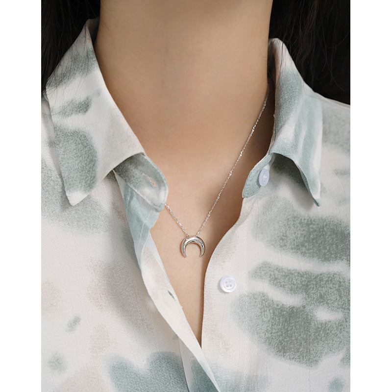 Necklace with a crescent moon pendant worn by a person in a light-colored shirt.