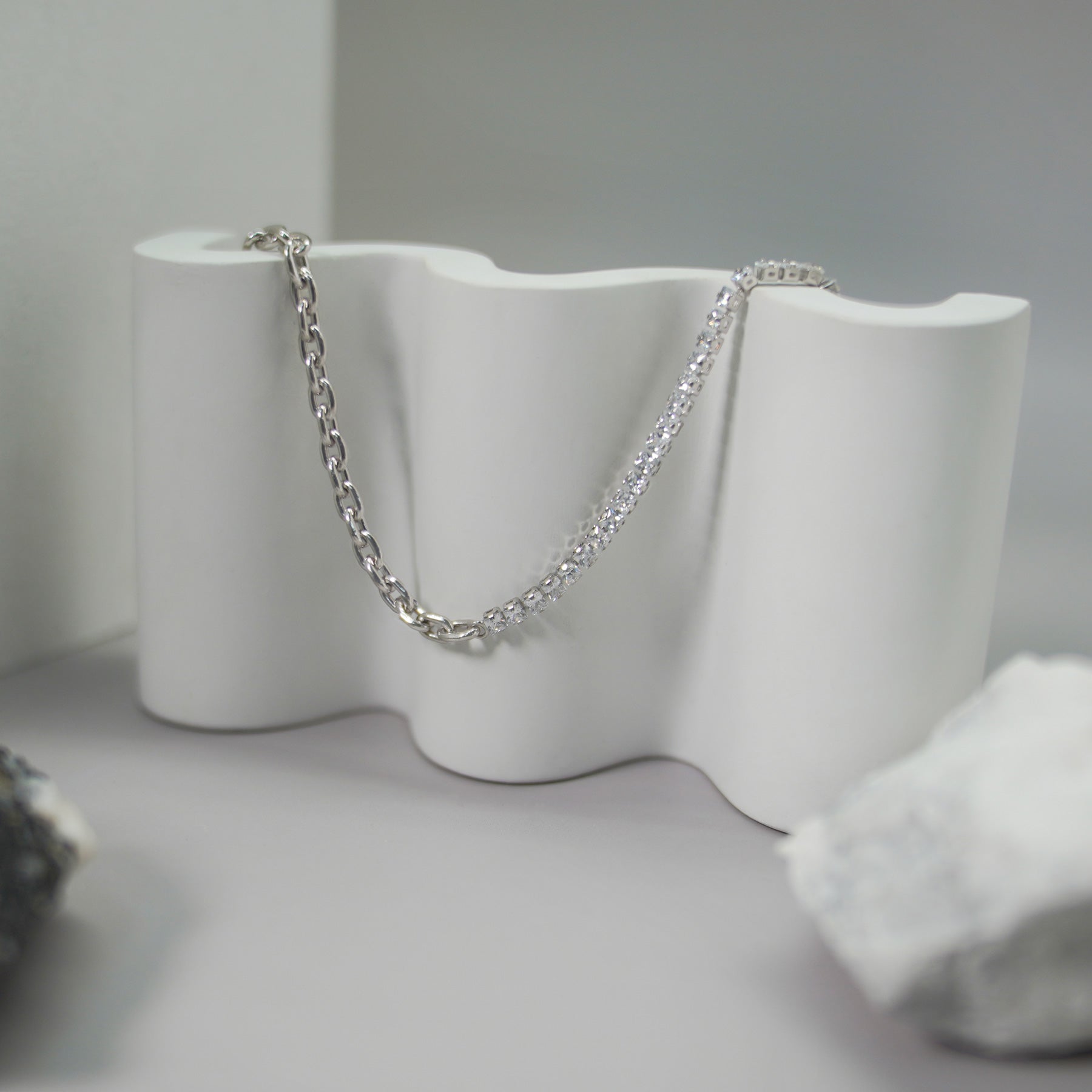 Silver chain draped over a white ceramic vase on a gray surface.