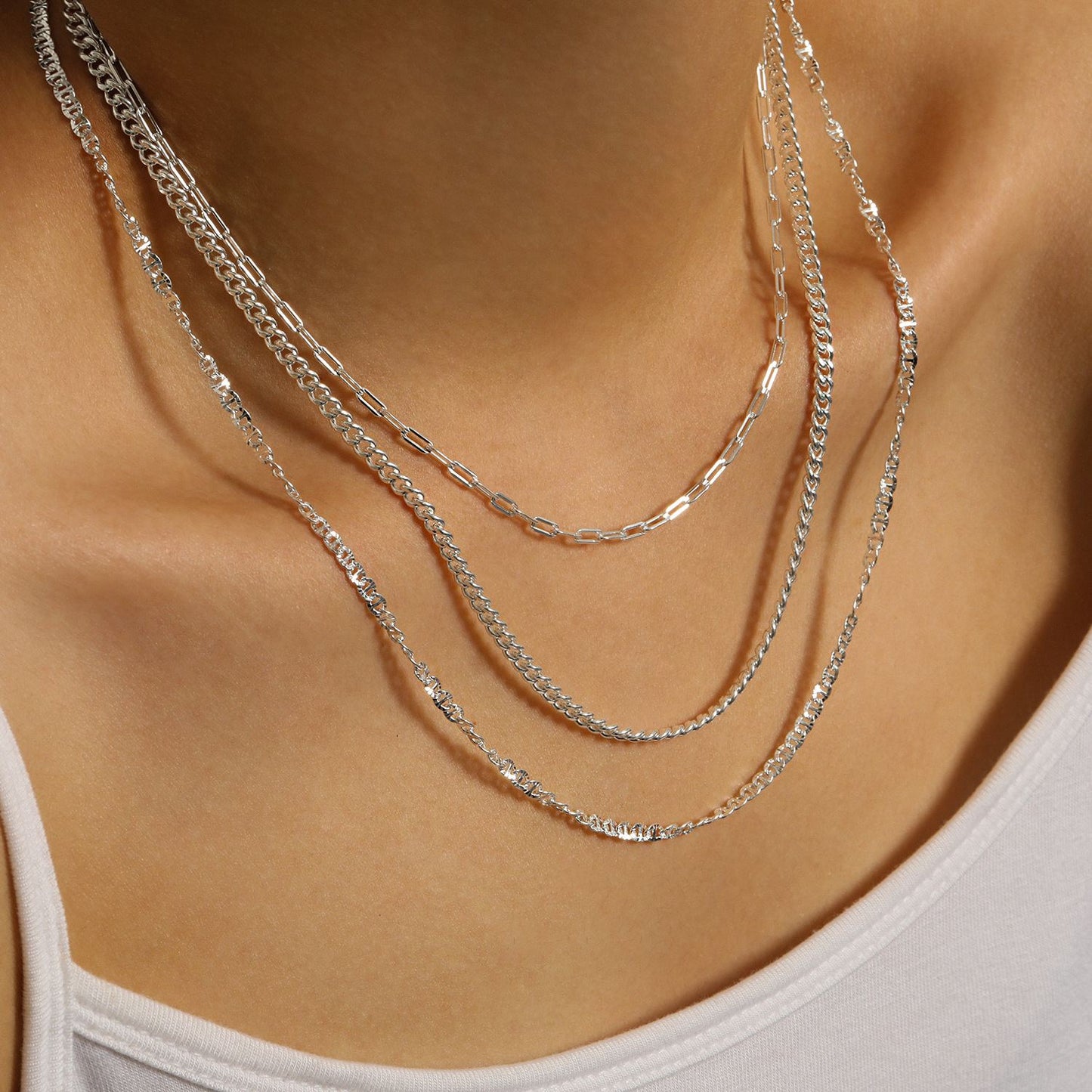Silver chain necklaces on a person wearing a white top