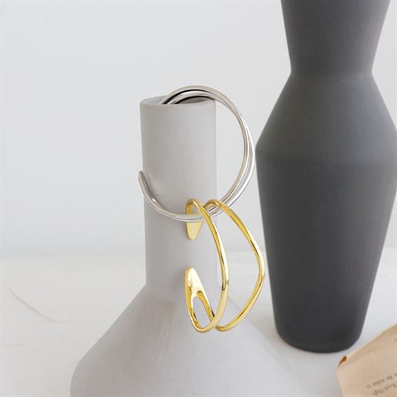 Gold and silver hoop earrings on a mannequin with a gray vase in the background