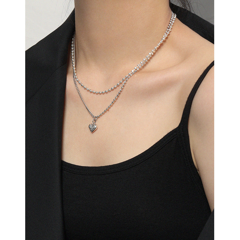 Person wearing a delicate silver necklace with a heart pendant on a plain background