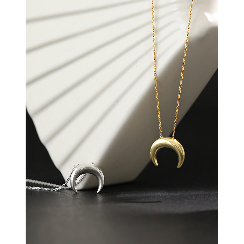 Two gold and silver crescent moon pendants on chains against a white ceramic dish.
