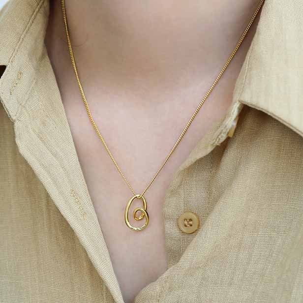 Gold necklace with a unique pendant worn by a person in a beige shirt.
