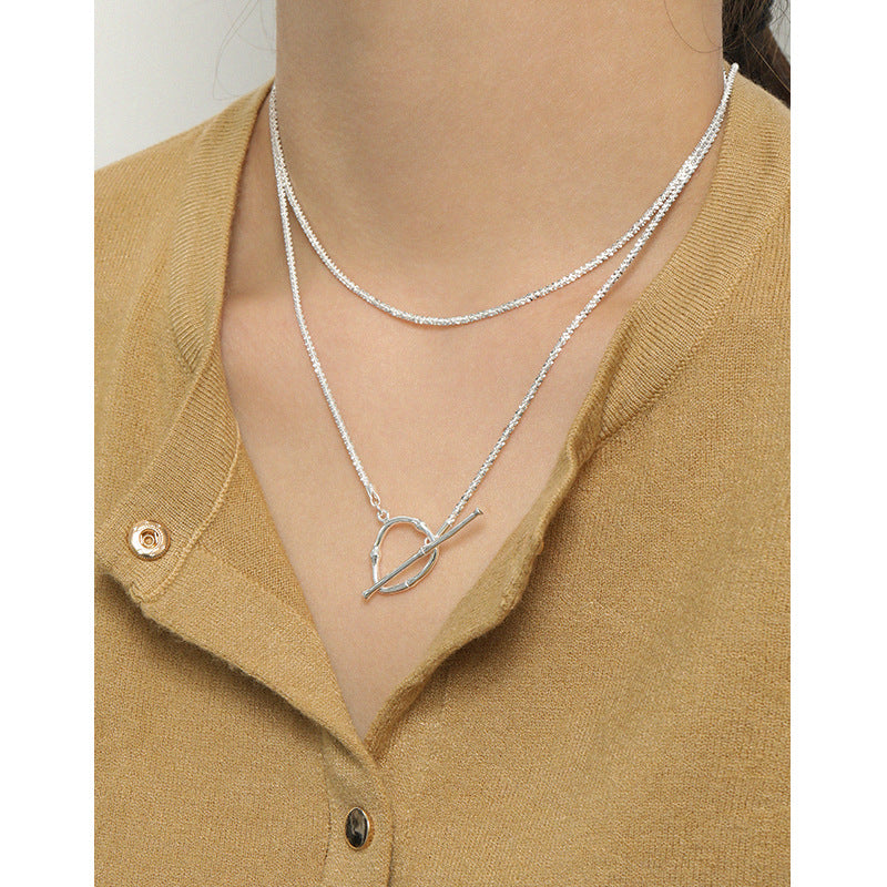 Silver necklace with a heart pendant worn by a person in a mustard yellow cardigan.