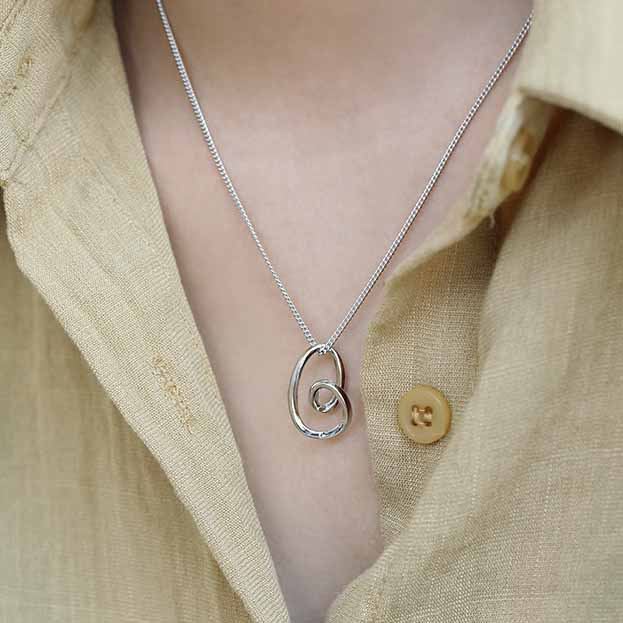 Silver necklace with a unique pendant worn by a person in a beige shirt.