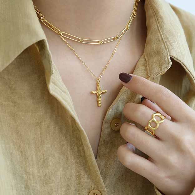Gold necklace with a cross pendant worn by a person in a beige shirt.