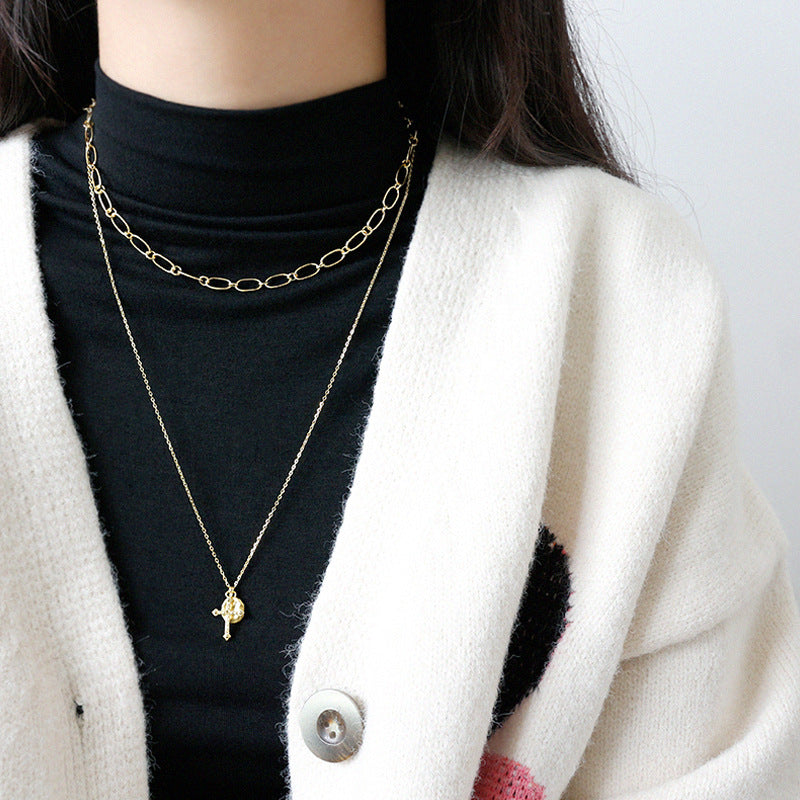 Person wearing a gold necklace with a small pendant against a neutral background