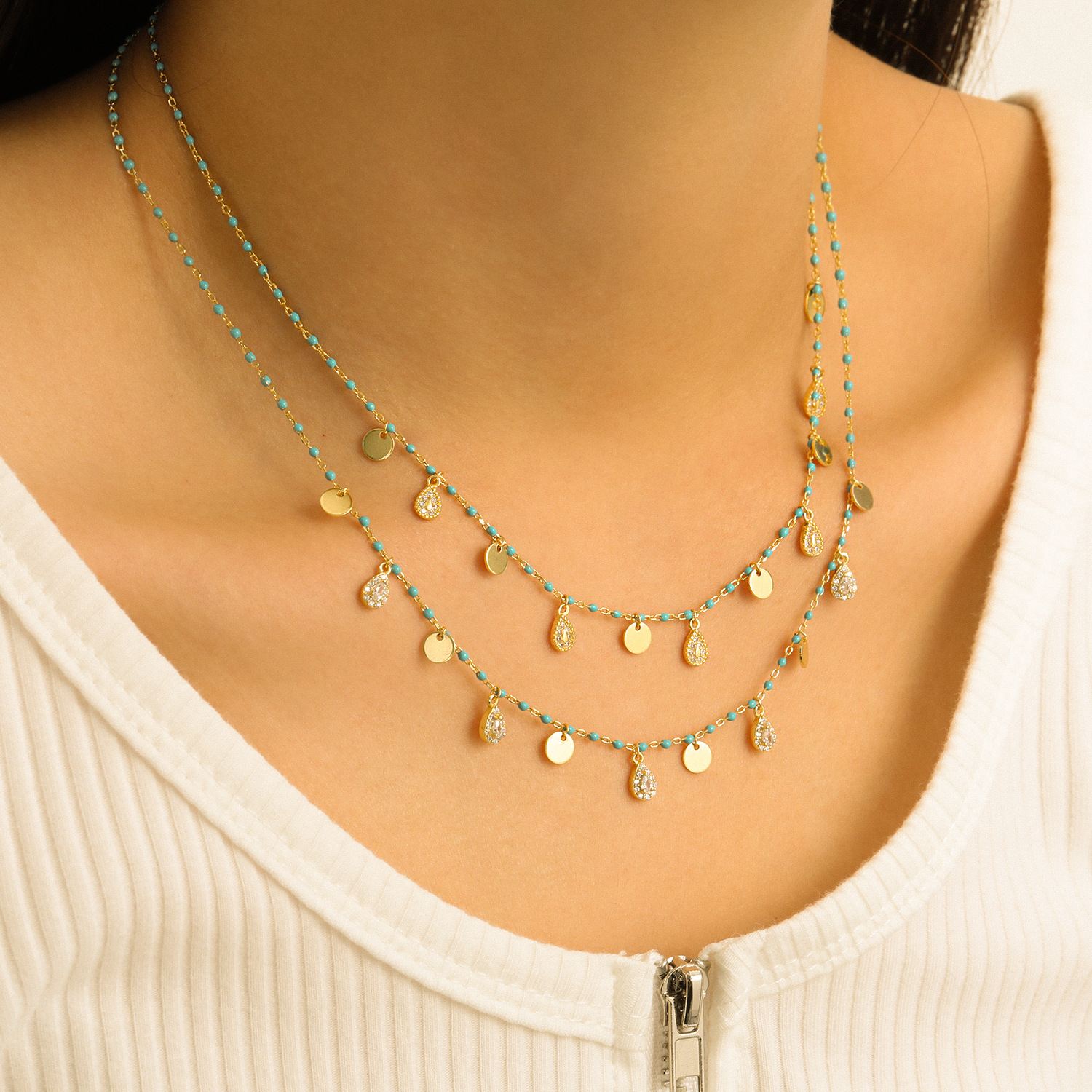 Necklace with gold and turquoise beads on a model wearing a white top.