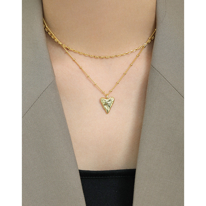 Gold necklace with a heart-shaped pendant worn by a person against a neutral background