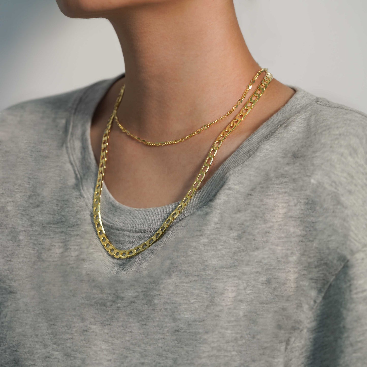 Person wearing a gold chain necklace on a plain background