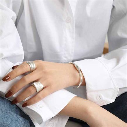 Close-up of a person wearing multiple rings on a white shirt background
