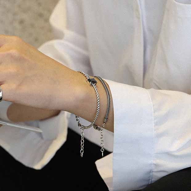 Close-up of a person's wrist wearing multiple bracelets on a white shirt background