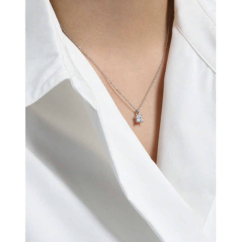 Silver necklace with a diamond pendant worn by a person in a white shirt.