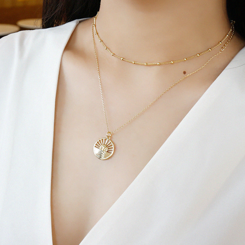 Gold necklace with a circular pendant worn by a person in a white outfit.