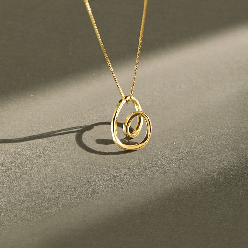 Gold necklace with a spiral pendant on a gray background
