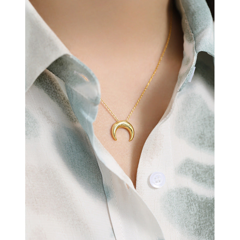 Gold necklace with a crescent moon pendant worn by a person in a light blue shirt.