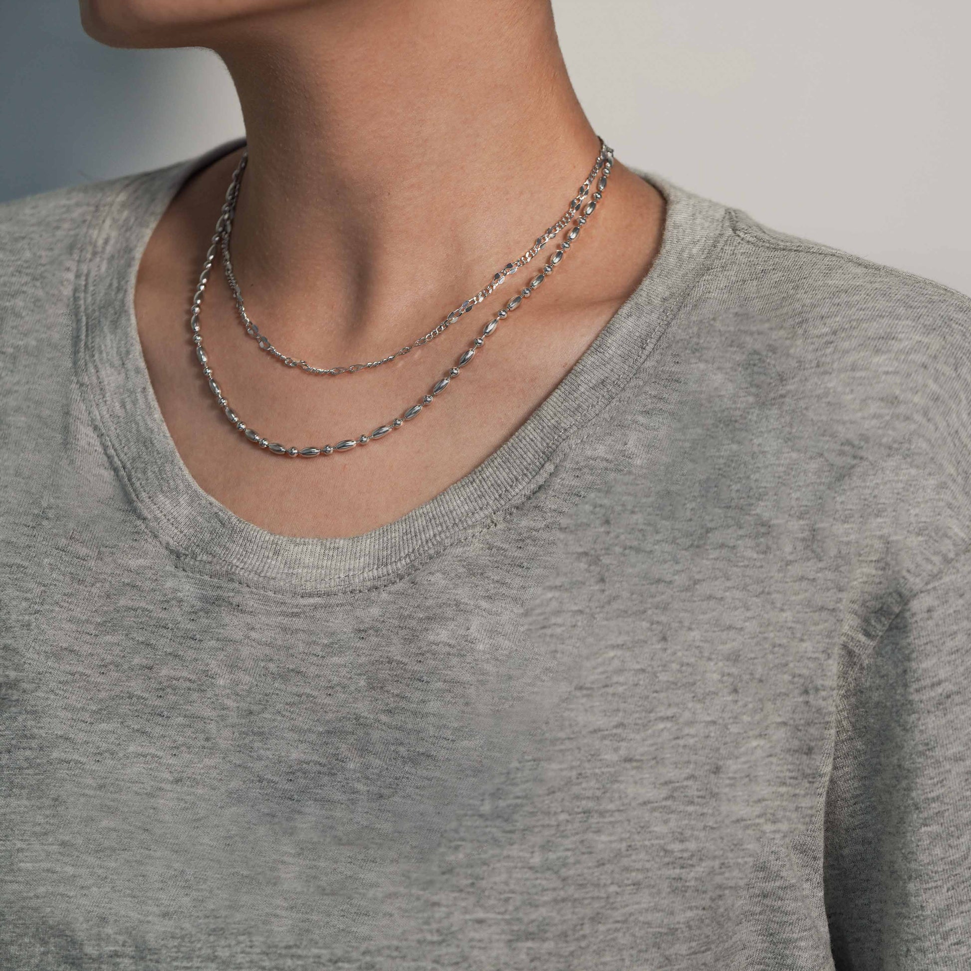 Person wearing a gray shirt with layered necklaces