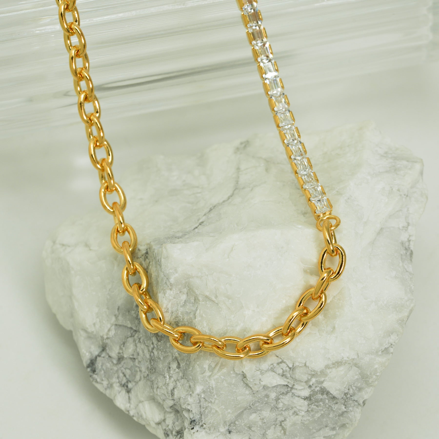 Gold chain necklace with a clear stone on a marble surface