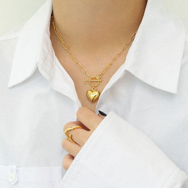Gold necklace with a heart pendant worn by a person in a white shirt.