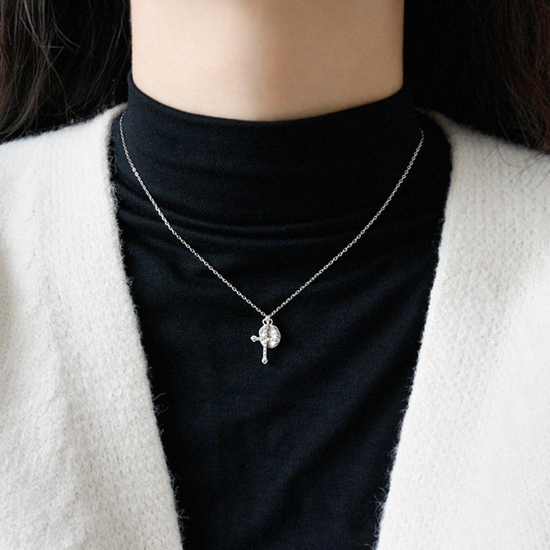 Person wearing a silver necklace with a pendant on a black turtleneck.