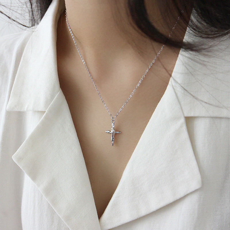 Silver cross necklace worn by a person in a white outfit