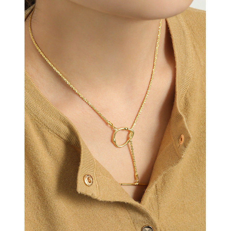 Gold necklace with a unique pendant worn by a person in a beige cardigan.