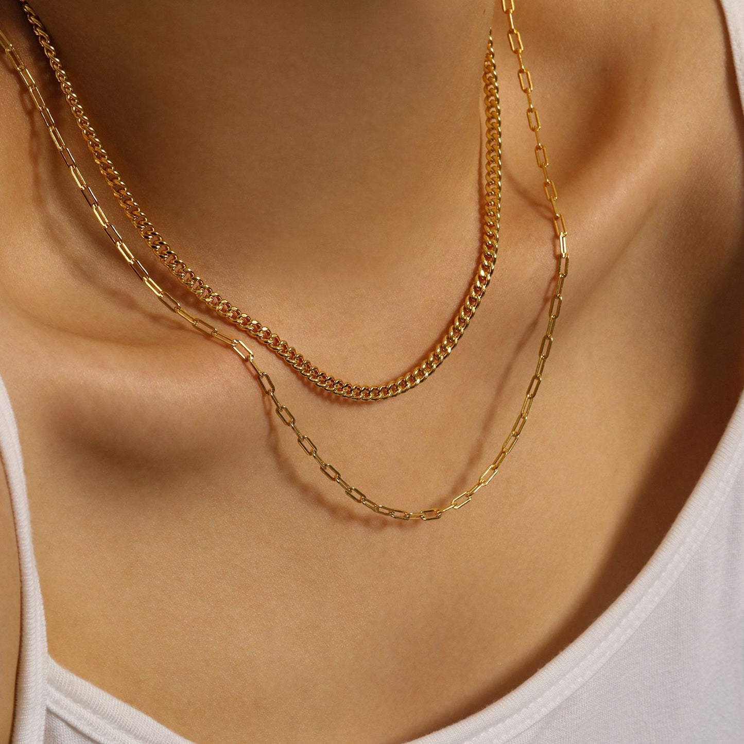 Two gold necklaces on a person wearing a white top.