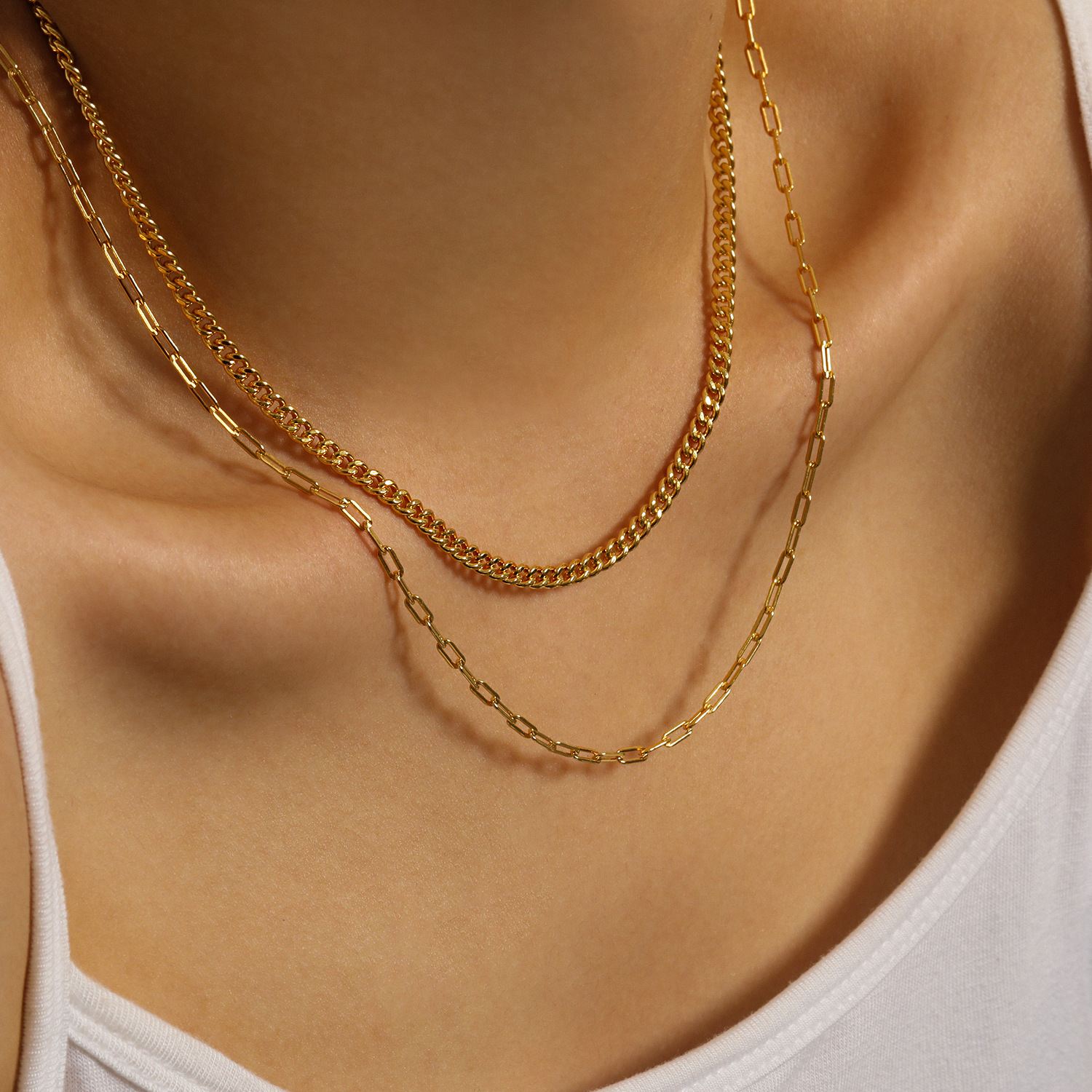 Two gold necklaces on a person wearing a white top.