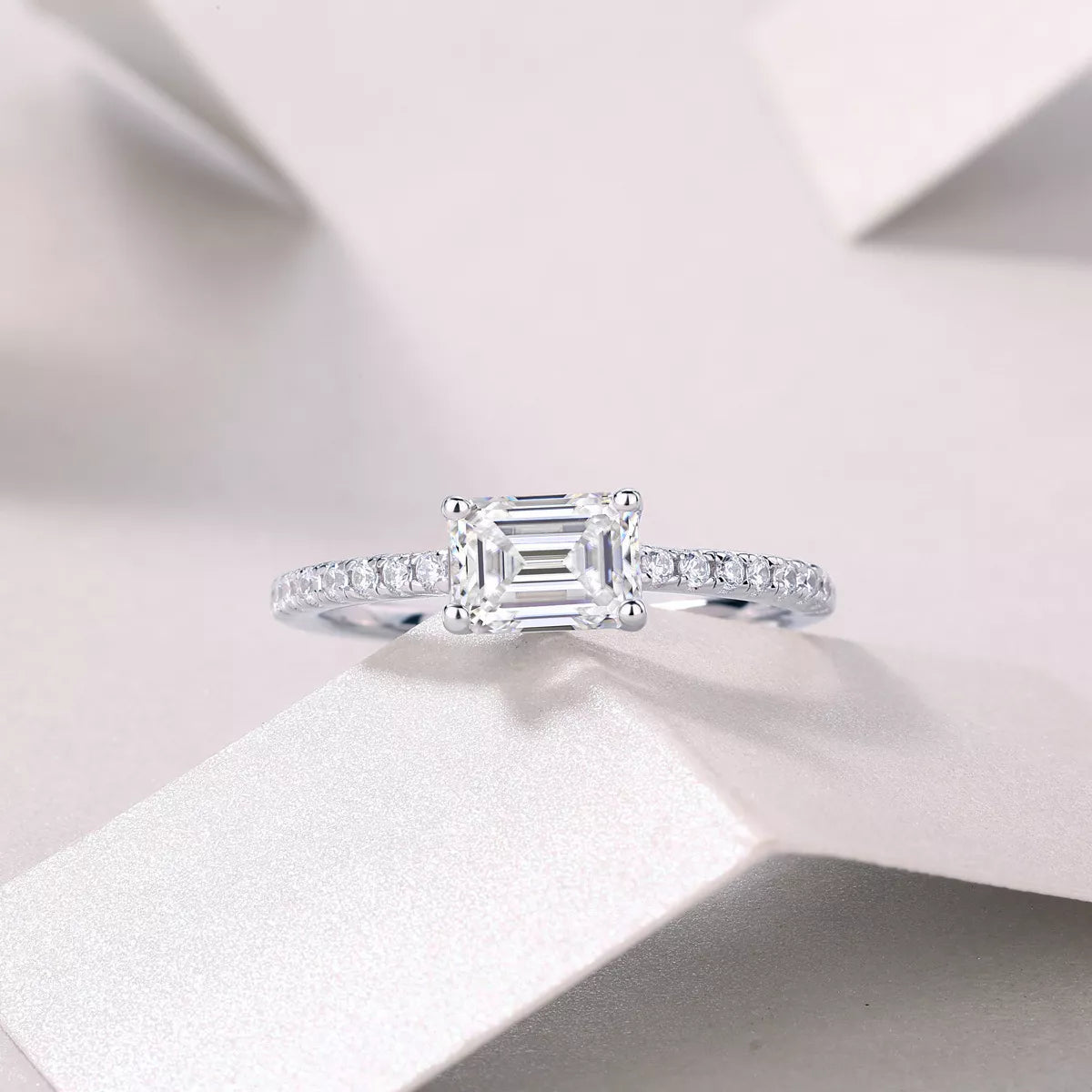 Diamond ring with emerald-cut center stone on a soft white background