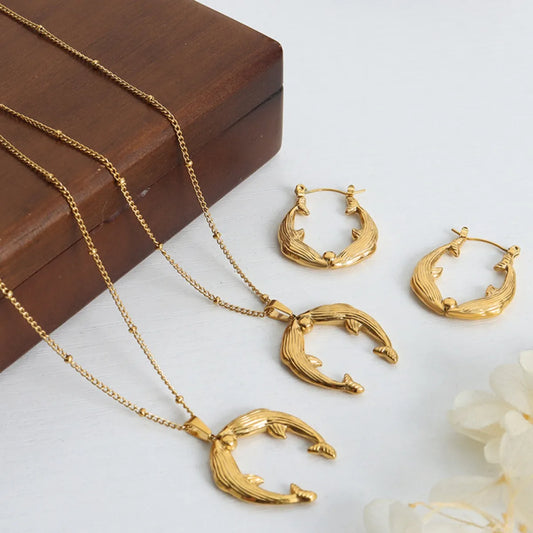 Gold necklace and earrings on a white surface with a wooden box in the background.
