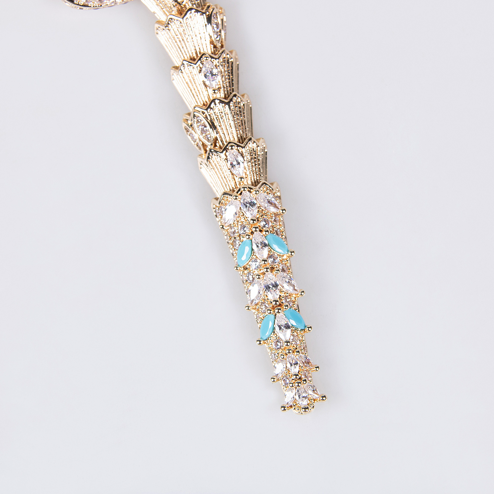 Close-up of gold snake jewelry with turquoise blue and clear stones on a light background.