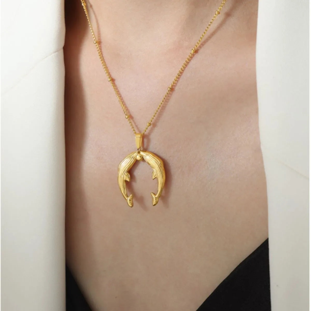 Gold necklace with a unique pendant on a person wearing a white outfit.