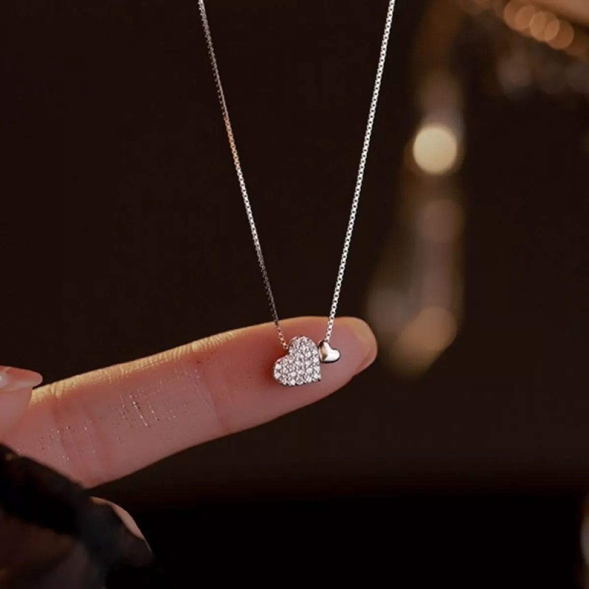 Silver necklace with heart pendants held between fingers against a dark background