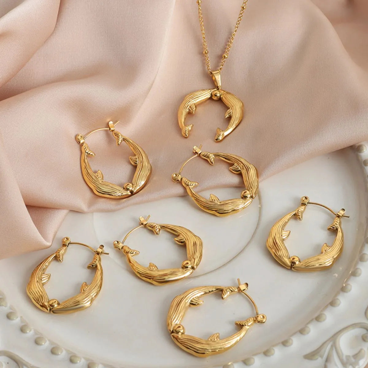 Gold hoop earrings and necklace on a decorative plate with soft fabric background